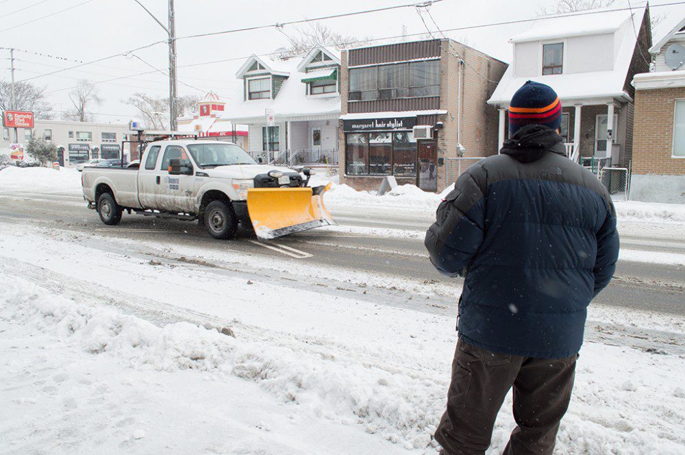 A snow truck drives by a bus stop after yet another snow storm.