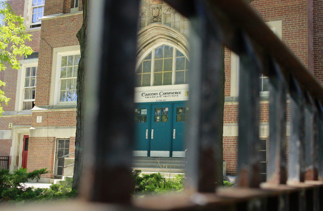 Shows the front doors of Eastern Commerce Collegiate Institute through metal bars.