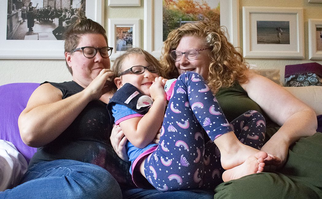 Merlin Hargraves (left) and Helen Hargreaves (right) cuddle their child, Eleanore on their couch.