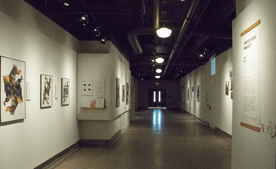 An empty hallway of the Forbidden Forest exhibit with white walls, a brown reflective floor, protratis on the walls and a door at the end of the hallway.