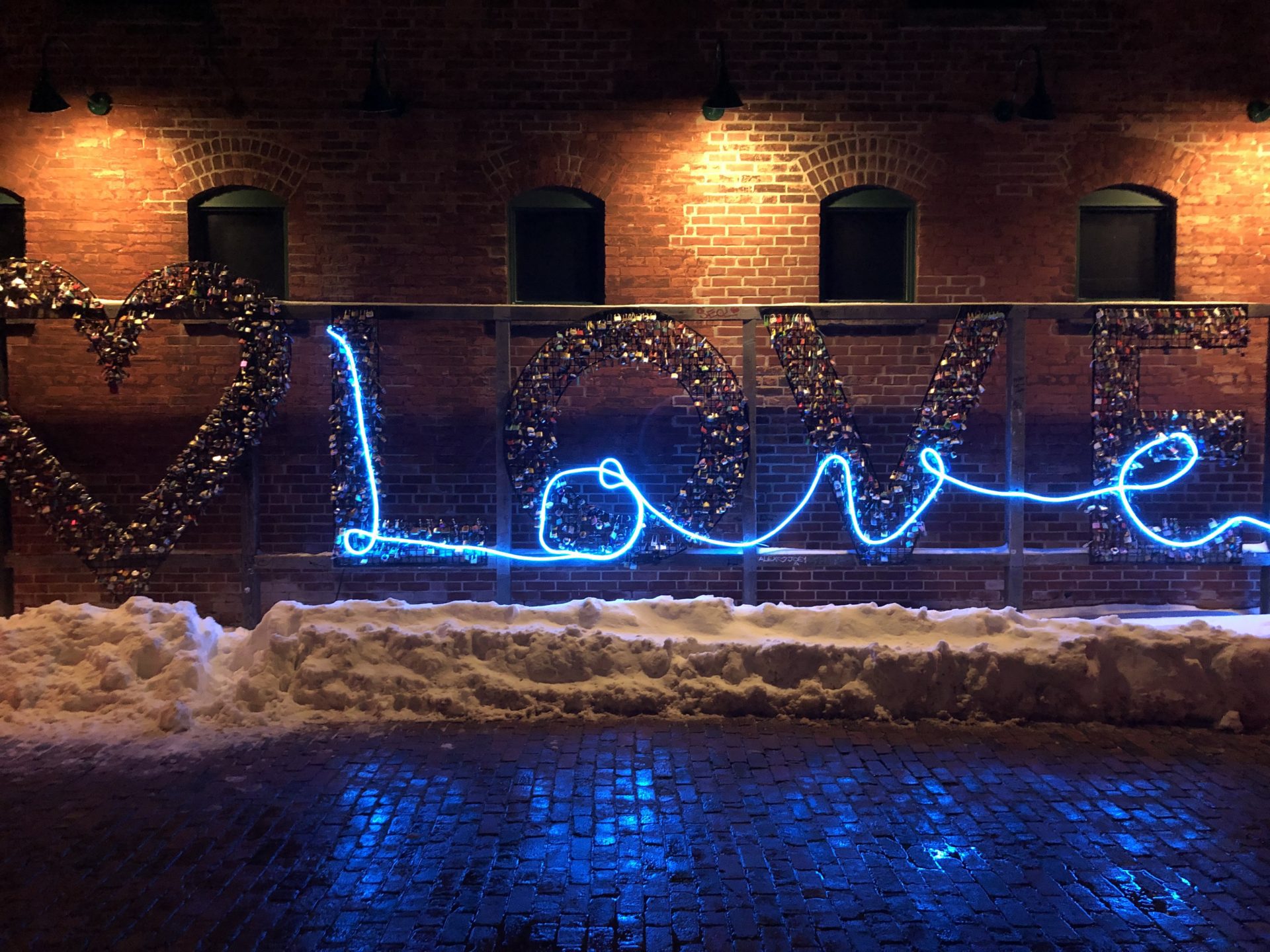A light installation at Toronto Light Fest spells "Love" in blue light and has locks surrounding it.