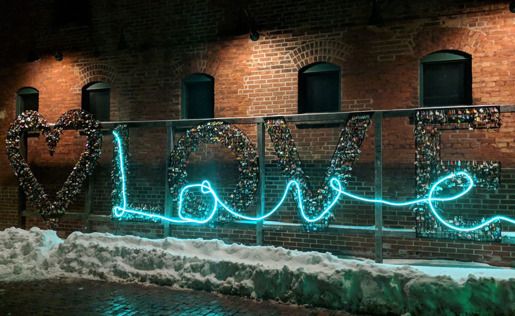 Art installation spells out the word "love" with metal, locks, and neon light.