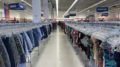 The aisle of a Toronto thrift store with shorts and shirts on the racks and patrons roaming the store.
