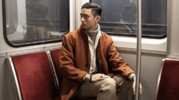 A man with an orange coat stares at a corner in a TTC subway train.