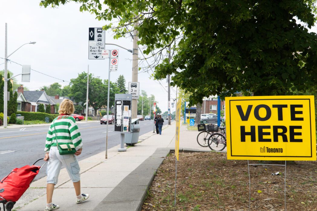 A person walks past a 'Vote Here' sign on the lawn of an advance polling station in East York