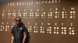 a server at Toronto's O'noir restaurant, stands in front of wall art depicting the Braille alphabet.