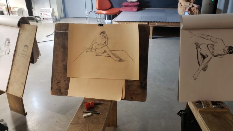A finished student sketch with pencil of a nude model on a wooden easel.