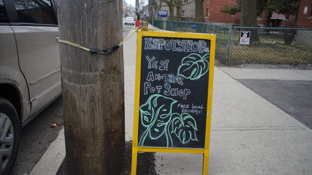 A sign for a cannabis shop stands on the sidewalk beside a wooden hydro pole