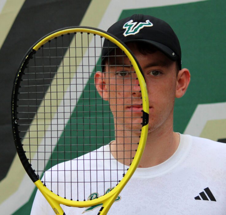 Ben Hudson holds a tennis racquet to his face
