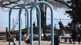 4 kids on the swings at a playground with the beach in the background