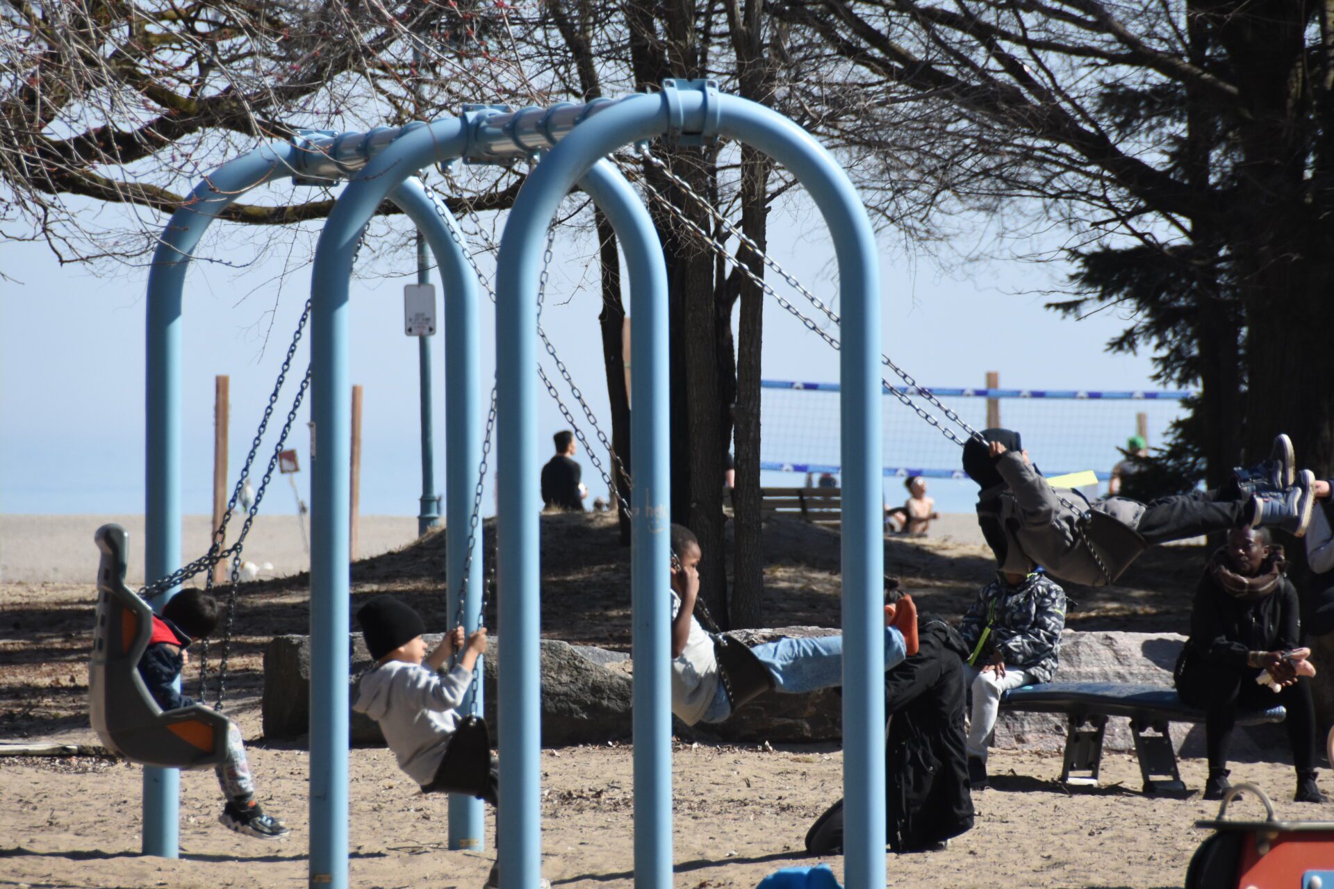 4 kids on the swings at a playground with the beach in the background