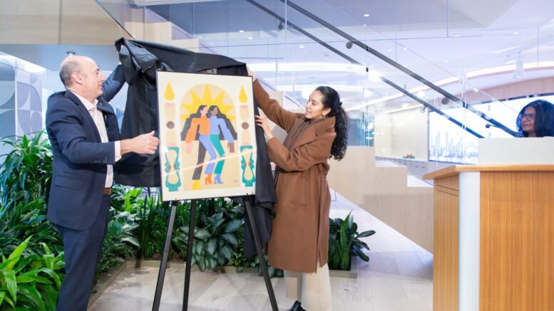 A woman unveils a painting in a lobby.