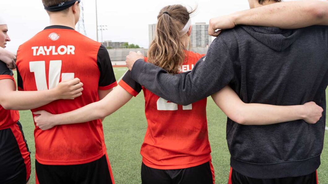 A quadball player puts her arms around her teammates' shoulders on the field.